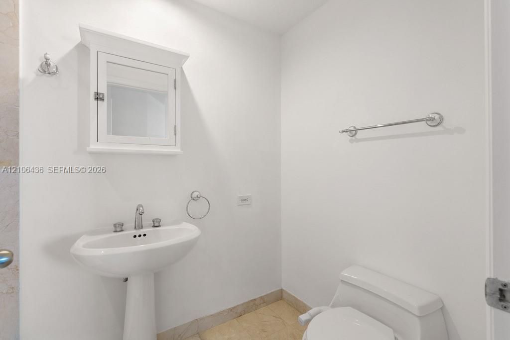 Pedestal sink with polished chrome fixtures, wall-mounted medicine cabinet with crown molding, and stone-finish flooring