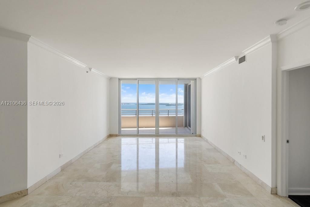 Living area featuring polished stone flooring, crown molding, and floor-to-ceiling glass sliding doors opening to a private balcony