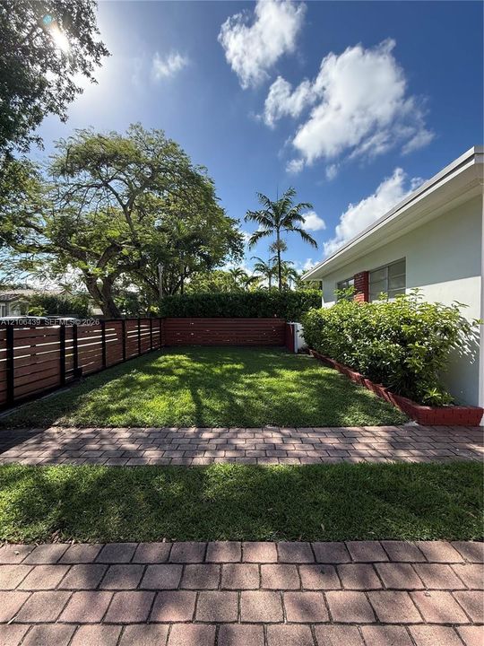 Backyard featuring a manicured lawn, horizontal wood-slat fencing, stone paver walkways, and mature landscape hedging