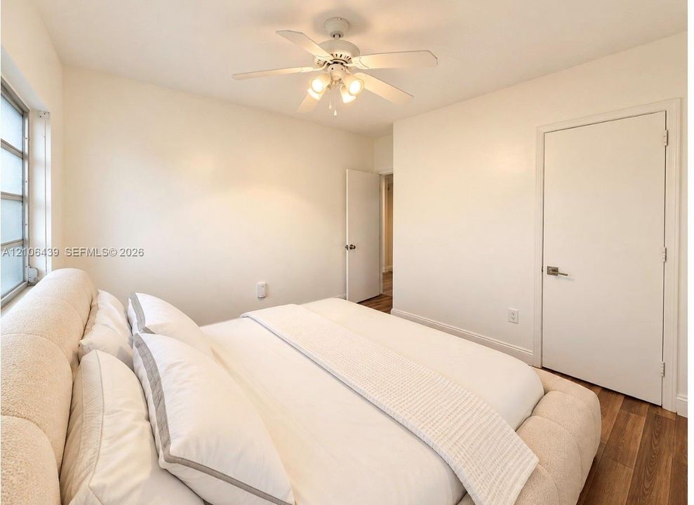 Neutral interior space featuring wood-finish flooring, a ceiling fan with integrated lighting, and white interior doors