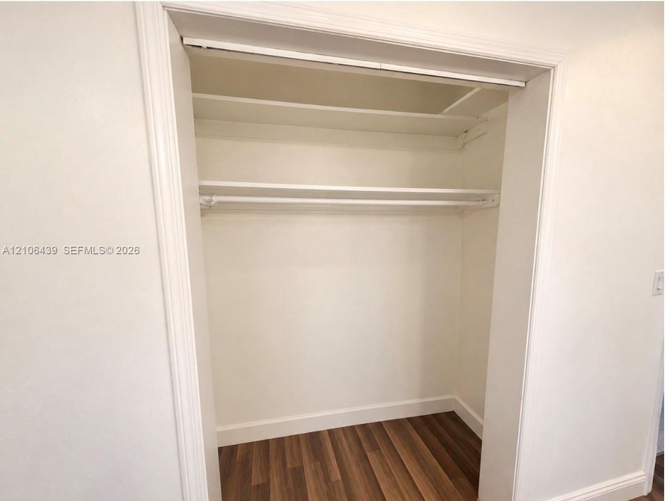 Built-in closet featuring wood-finish flooring, two upper shelves, and a metal hanging rod framed by white casing