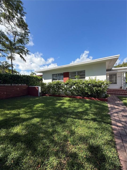 Single-story exterior featuring white stucco siding, red brick accent detailing, a paved walkway, and a landscaped lawn