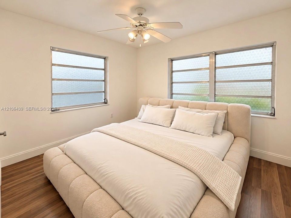 Wood-finish flooring, multi-pane jalousie windows, and a central ceiling fan with integrated lighting