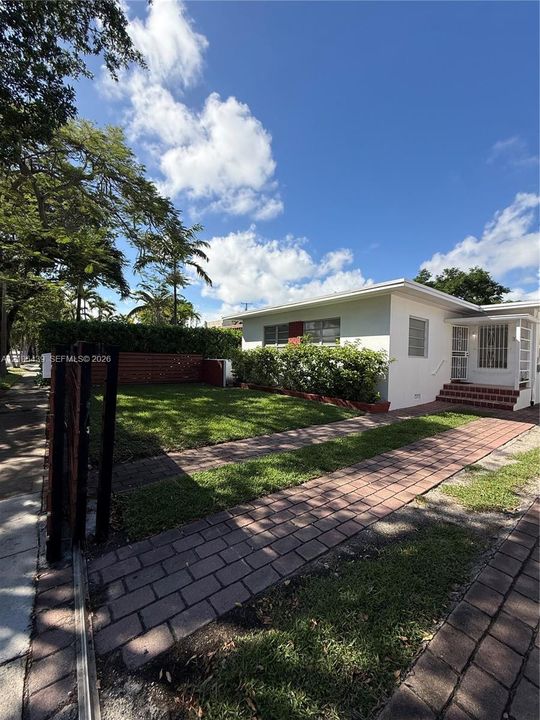 Exterior facade with stucco finish, brick-paver walkway, manicured lawn, privacy-fencing, and built-in entry steps with brick treads