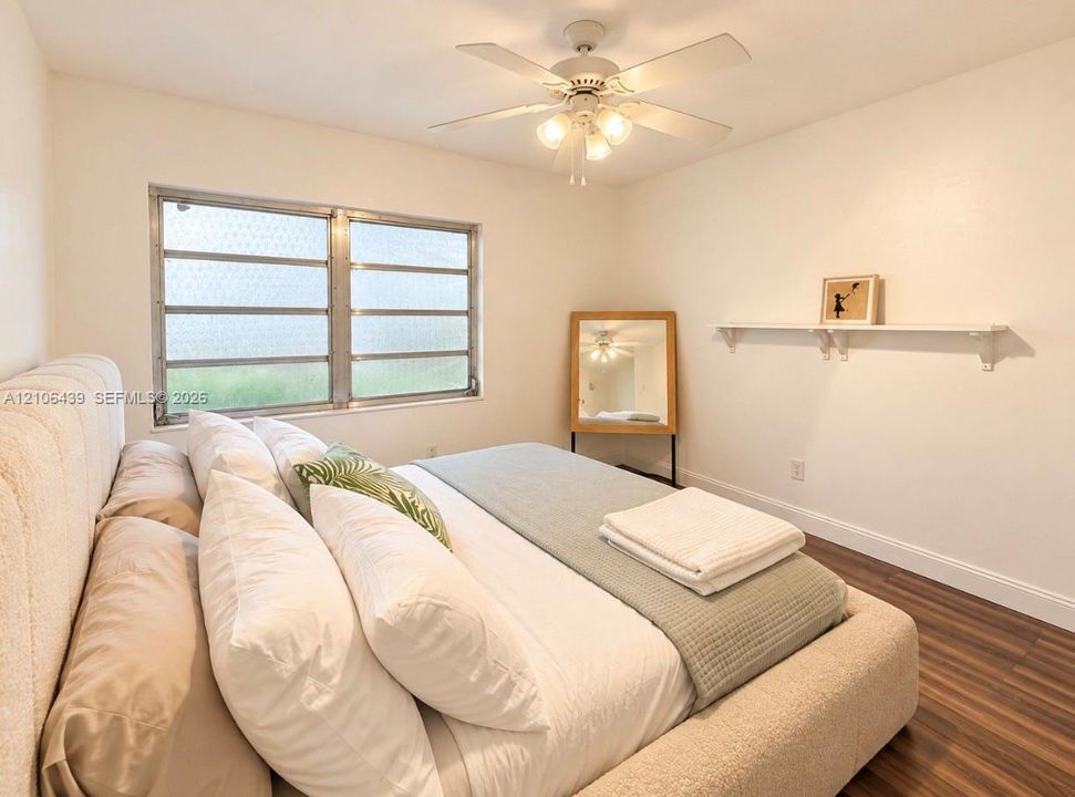 Room featuring wood-finish flooring, a wall-mounted floating shelf, and a ceiling fan with integrated lighting
