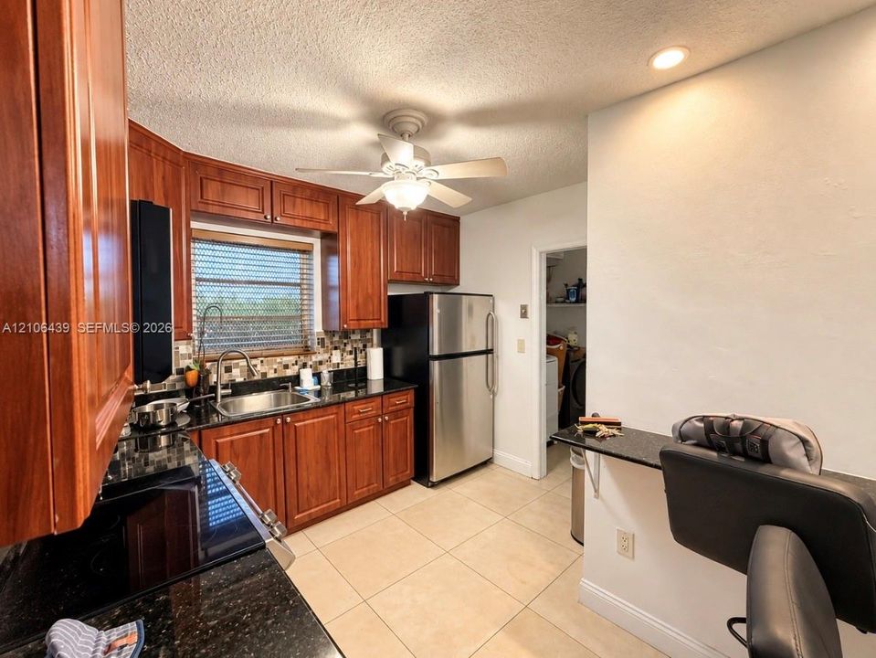 Kitchen featuring wood-finish cabinetry, dark stone countertops, mosaic tile backsplash, stainless steel appliances, and tile flooring