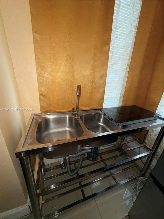 Stainless steel dual-basin utility sink, integrated two-burner electric cooktop, and open-frame metal shelving