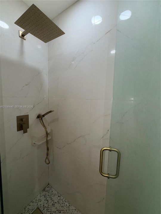 Shower enclosure featuring large-format veined wall tile, a rainfall showerhead, a separate handheld sprayer, a built-in shelf, and a glass door with metallic hardware