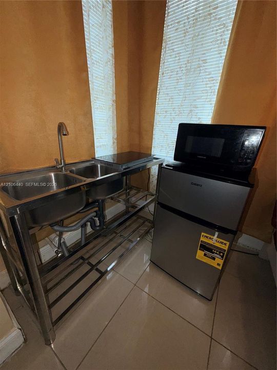 Stainless steel dual-basin sink with a gooseneck faucet, integrated metallic shelving unit, and tile flooring