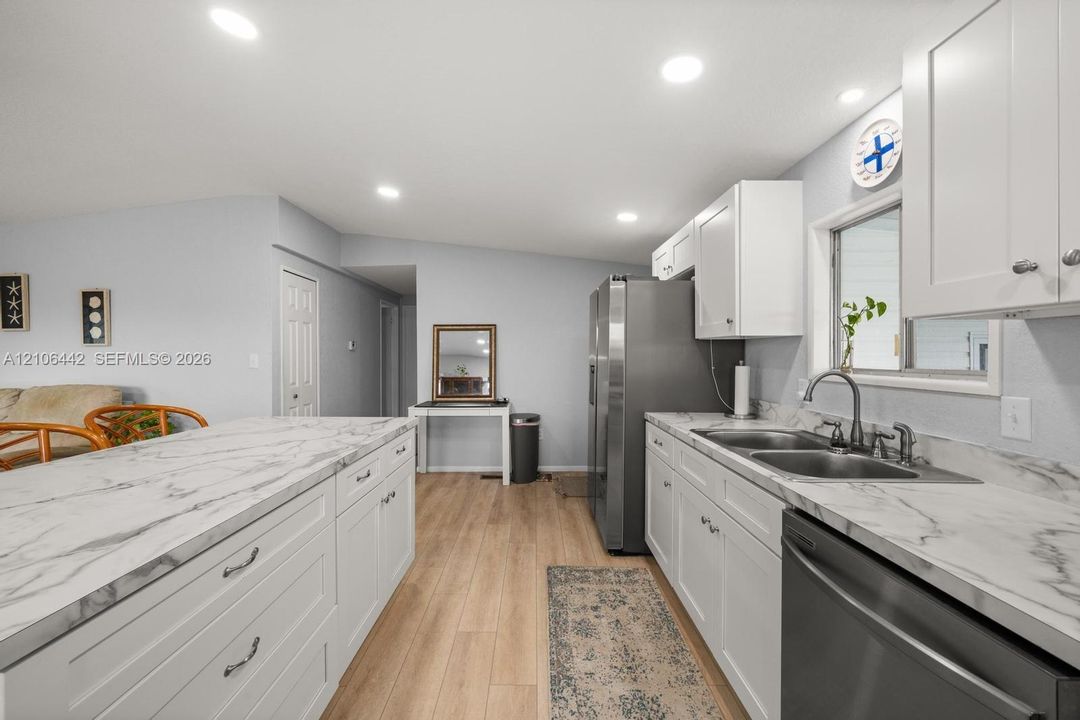 Kitchen featuring white cabinetry, stone-finish countertops, stainless steel appliances, a double-basin undermount sink, and wood-finish flooring