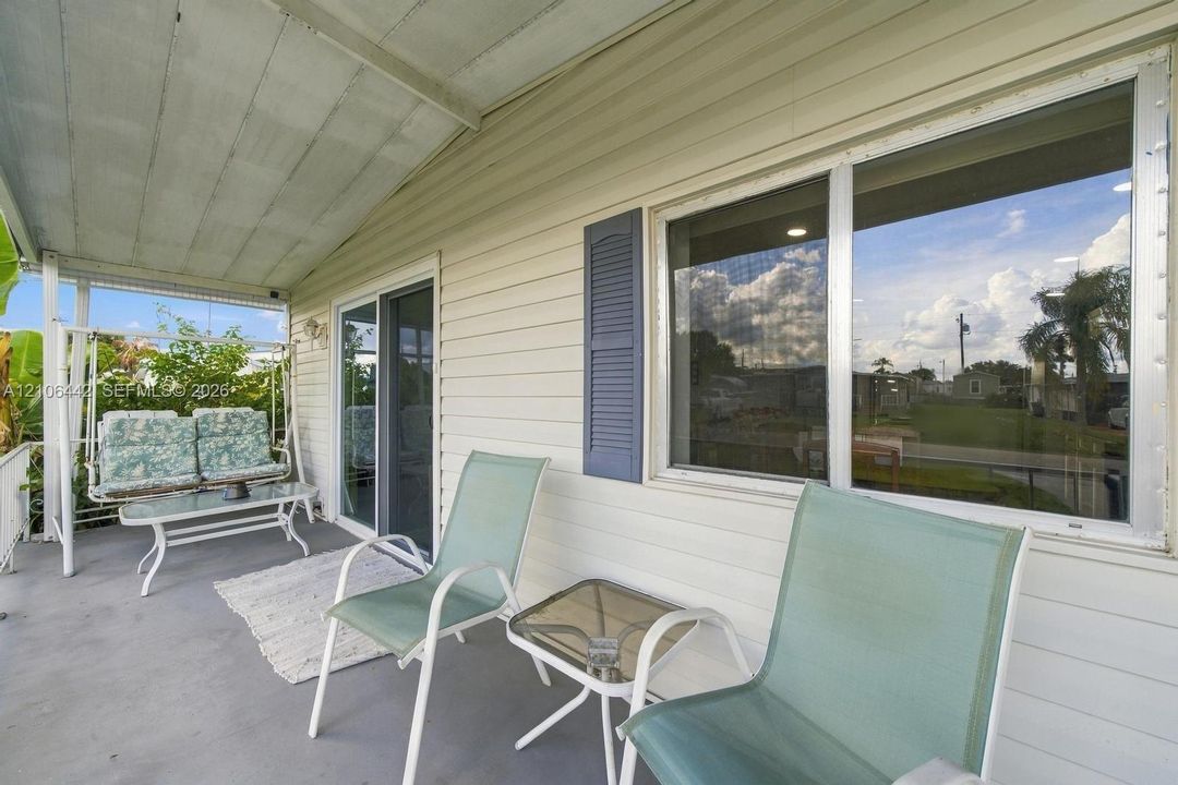 Covered exterior porch featuring light-colored horizontal siding, sliding glass doors, and a single decorative window shutter