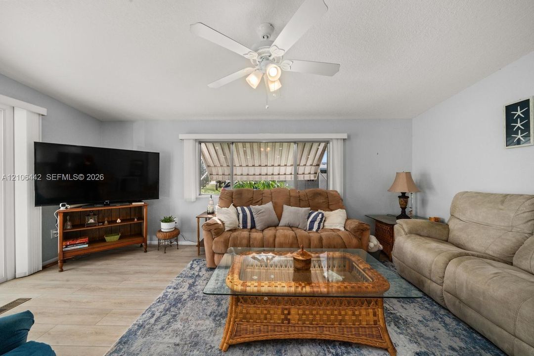 Living area featuring wood-finish flooring, a ceiling fan with integrated lighting, and a large window equipped with an exterior retractable awning