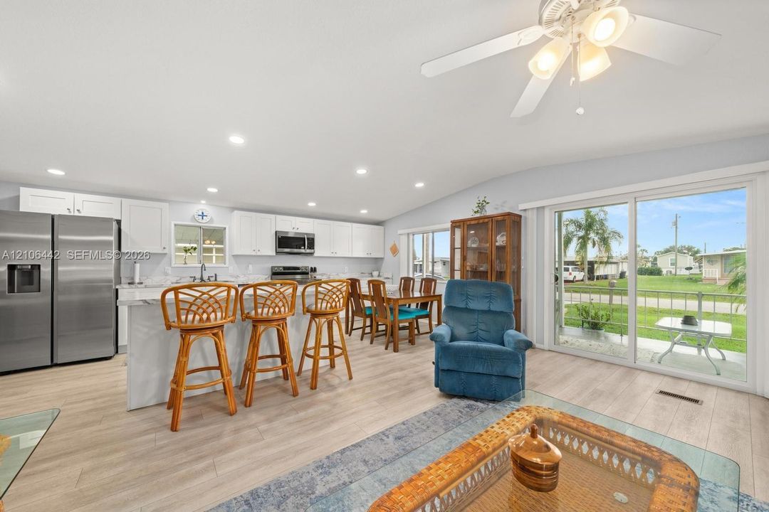 Open-concept kitchen featuring white cabinetry, wood-finish flooring, recessed lighting, stainless steel refrigerator, and sliding glass doors
