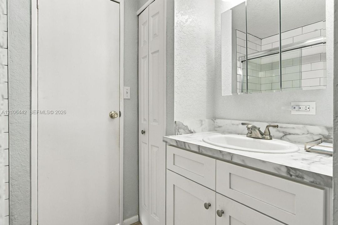 White vanity with stone-finish countertop, oval undermount sink, three-panel medicine cabinet, and tall storage closet with louvered doors