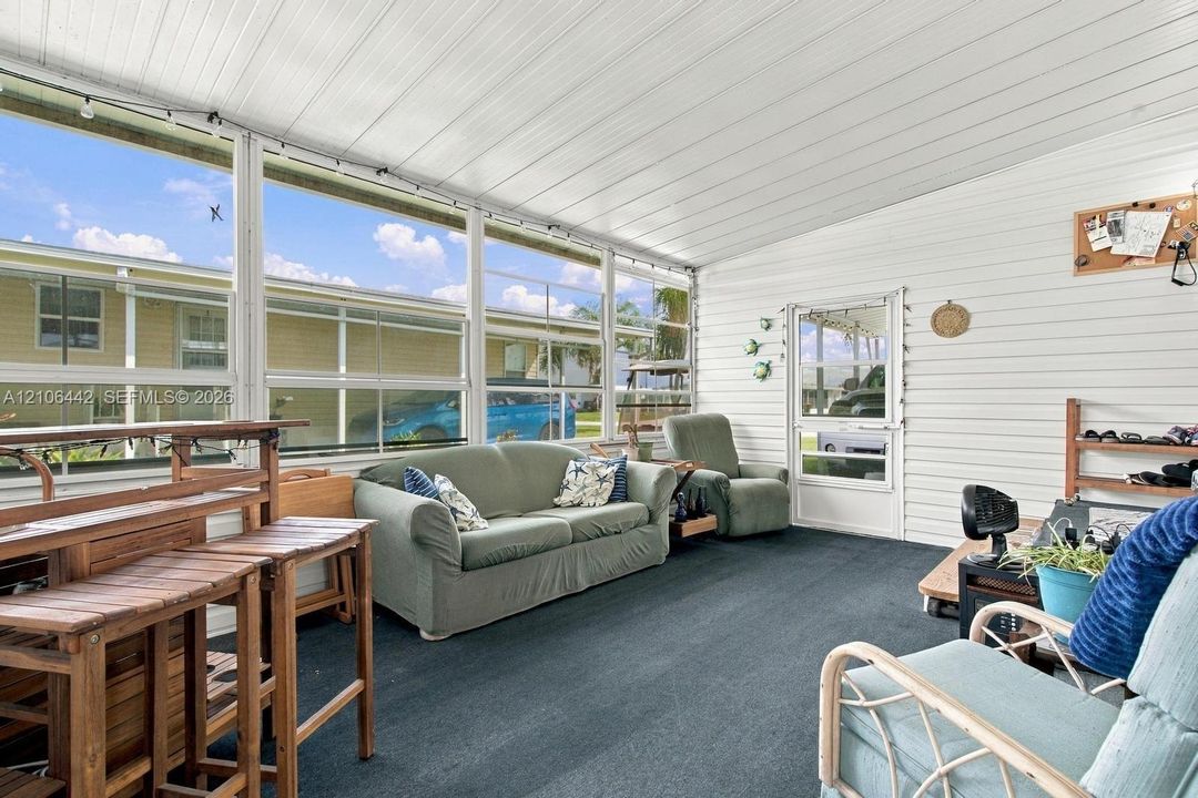 Enclosed patio featuring floor-to-ceiling screen panels, white horizontal siding, white beadboard-style ceiling, and a full-height glass entry door