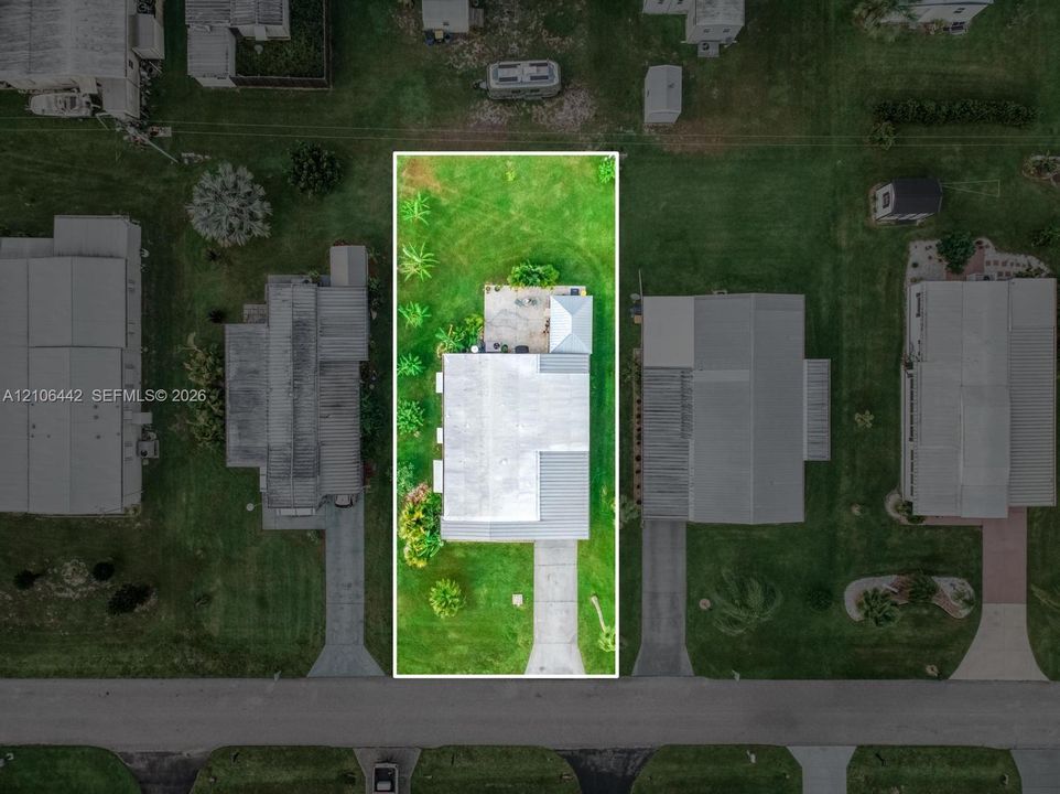 Aerial view featuring a rectangular lot, concrete driveway, rear patio, and mature landscaping