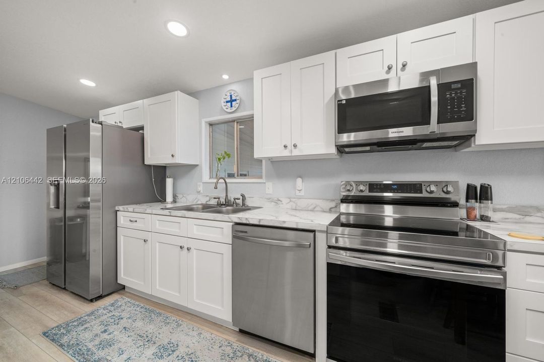 Kitchen featuring white shaker-style cabinetry, stone-patterned countertops, stainless steel appliances, and wood-finish flooring