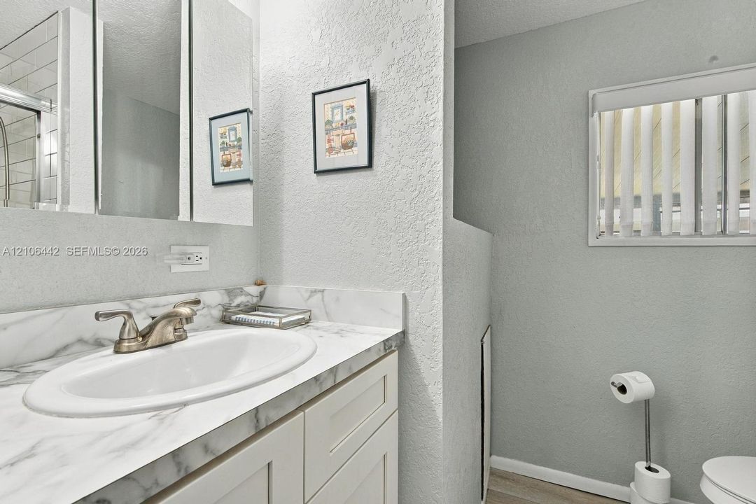 Vanity featuring an oval undermount sink, stone-patterned countertop, shaker-style cabinetry, and a mirrored medicine cabinet