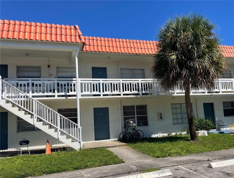 Two-story exterior featuring a terracotta-style tile roof, white stucco facade, and white wooden balcony railing with matching external staircase