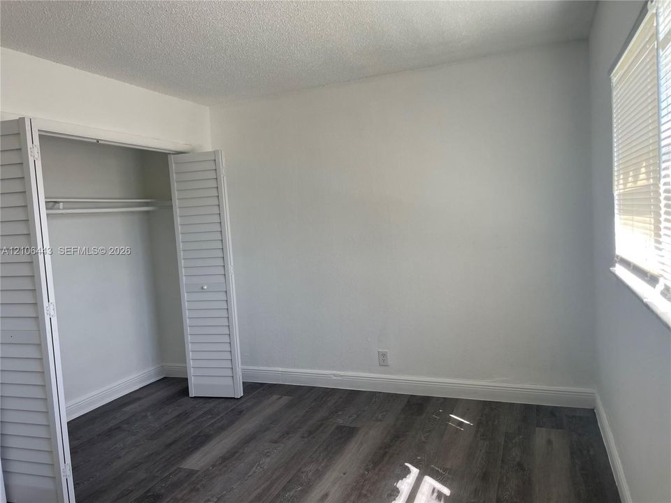 Room featuring wood-finish flooring, white walls, and a closet with louvered bifold doors
