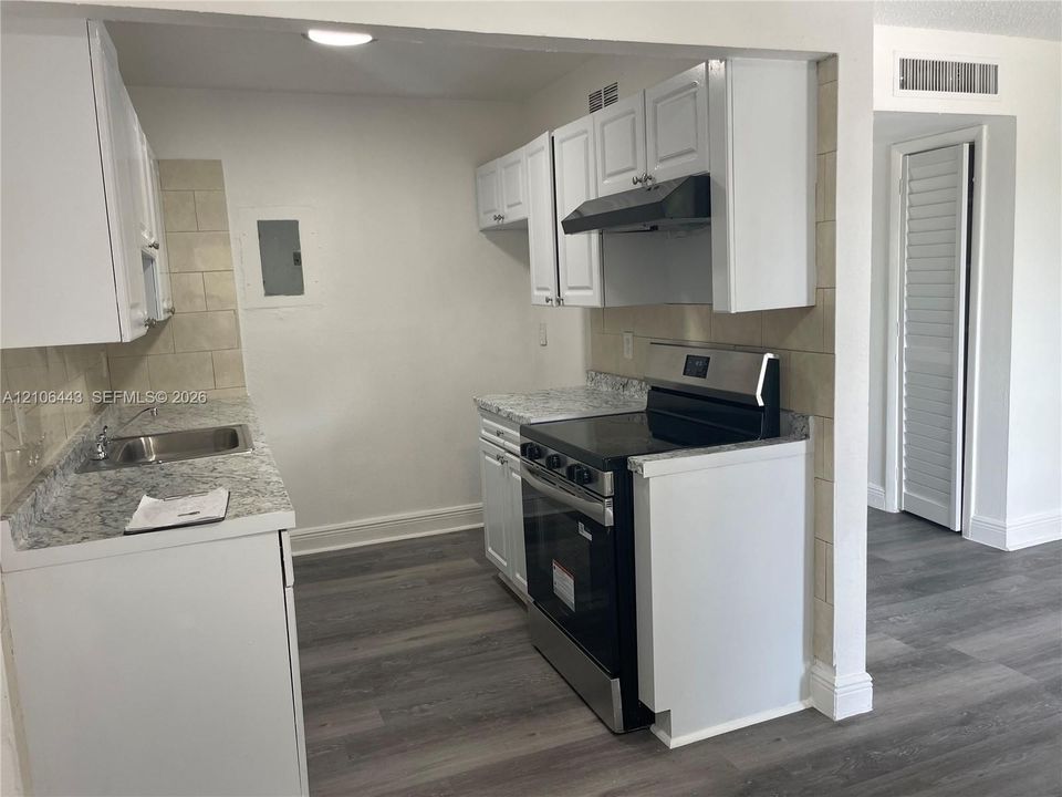 Kitchen featuring white cabinetry, stone-patterned laminate countertops, stainless steel range with integrated hood, stainless steel sink, and wood-finish flooring