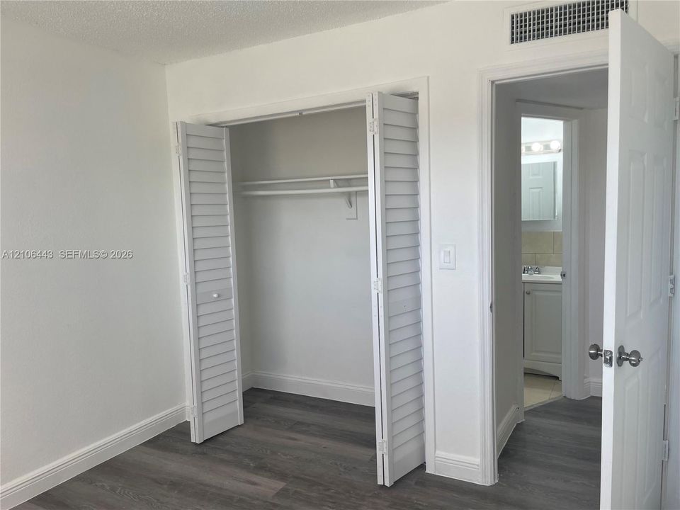 Interior space featuring wood-finish flooring, white louvered closet doors, and solid-core panel doors with brushed nickel hardware