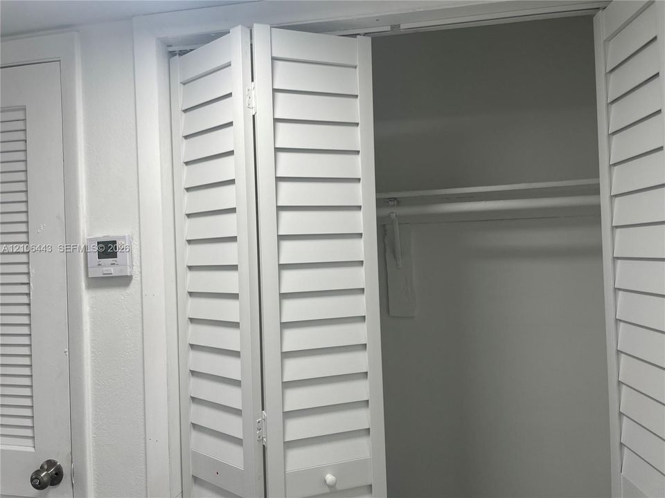 White bi-fold louvered closet doors, interior shelf, and metal garment rod