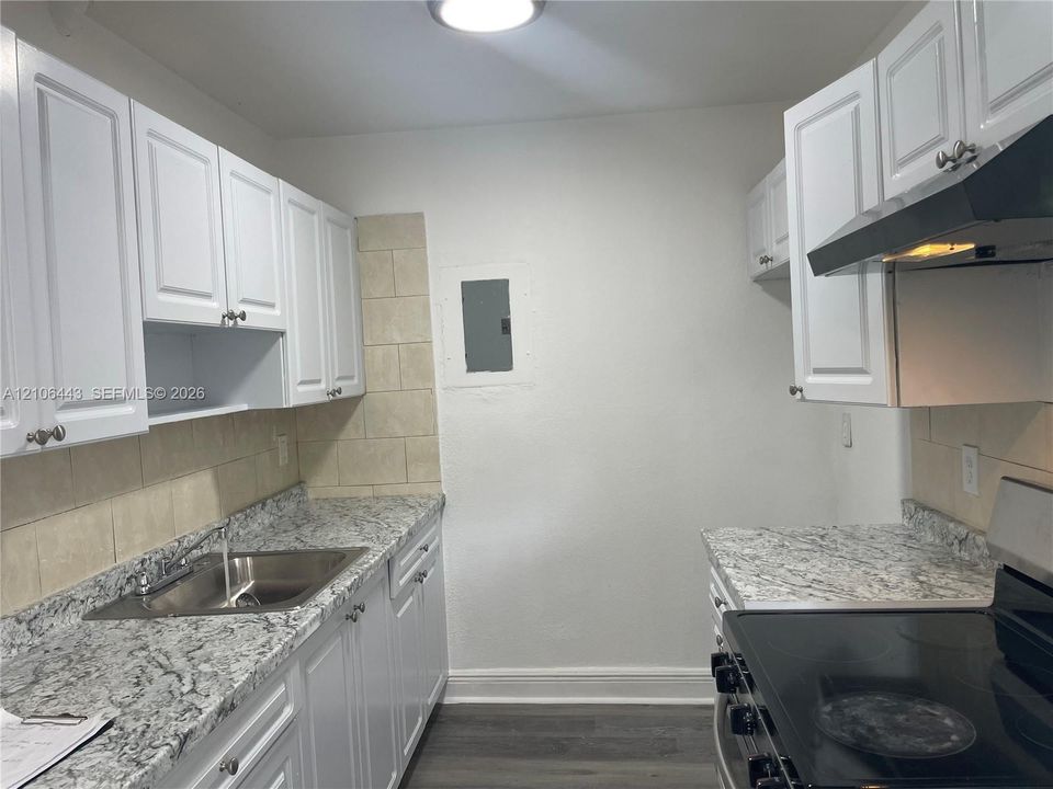 Kitchen featuring white cabinetry, stone-patterned countertops, a stainless steel sink with a mounted faucet, tile backsplash, and wood-finish flooring