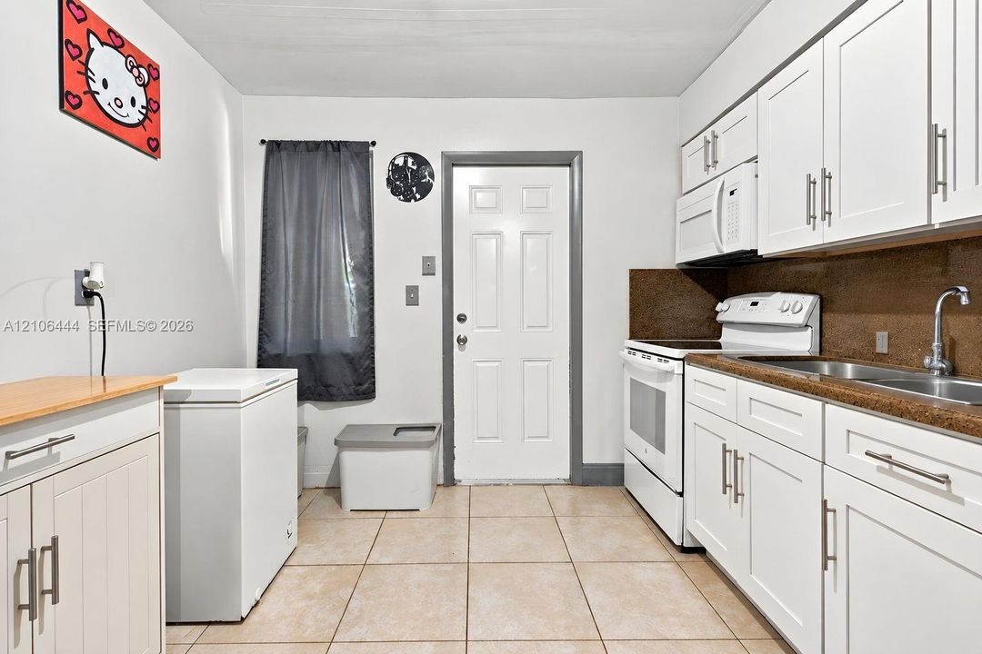 Kitchen featuring white shaker-style cabinetry, solid-surface countertops, tile flooring, and a stainless steel dual-basin sink