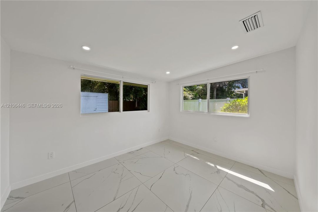 Large-format rectified tile flooring with veining, recessed lighting, and multiple windows providing natural light