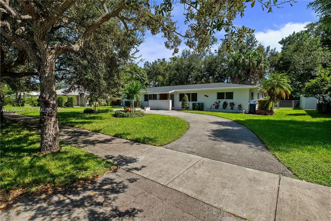 Single-story residence featuring a painted masonry exterior, a curved asphalt driveway, and expansive lawn area with mature landscaping