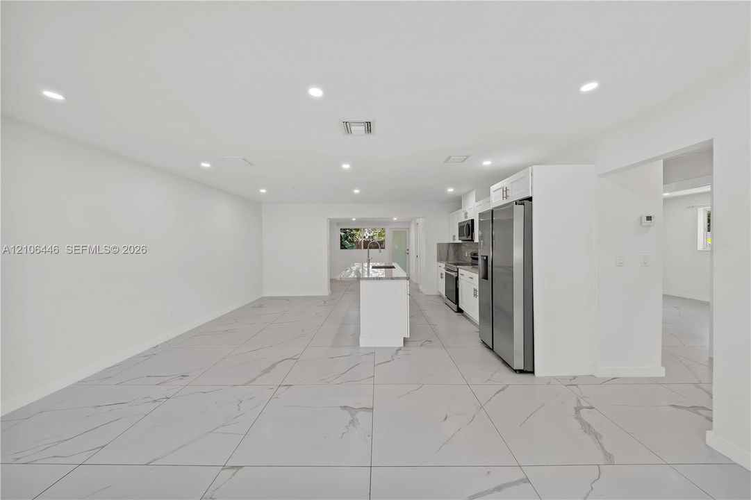Kitchen featuring large-format tile flooring with veining, white cabinetry, a center island with a stone-finish countertop, and recessed ceiling lighting