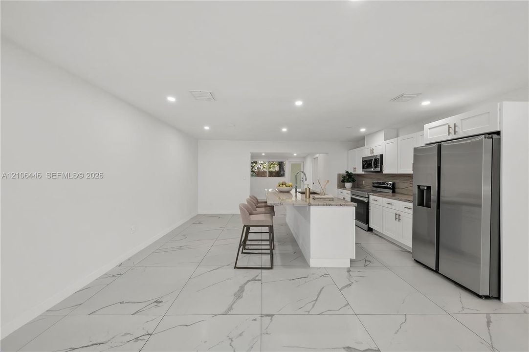 Kitchen featuring white cabinetry, stone-surface countertops, stainless steel appliances, a center island, and large-format tile flooring