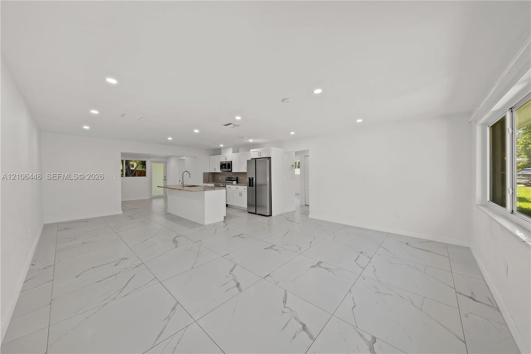 Open-concept area featuring large-format stone-patterned tile flooring, recessed lighting, and a kitchen equipped with a central island, stone-surfaced countertops, and stainless steel appliances