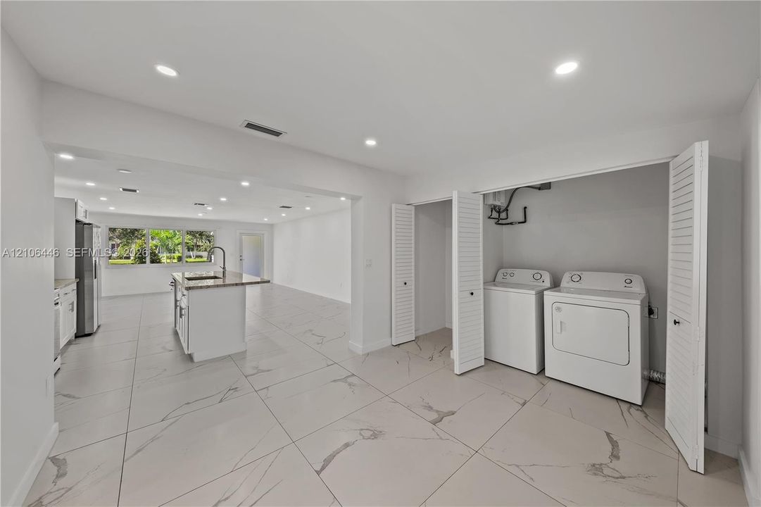 Large-format tiled flooring, recessed ceiling lighting, louvered closet doors, and kitchen island with an integrated sink