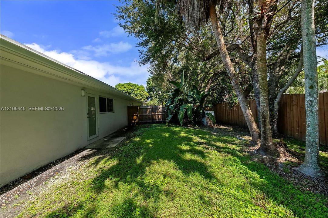 Rear exterior featuring a grass lawn, mature trees, wood privacy fencing, and a side access door