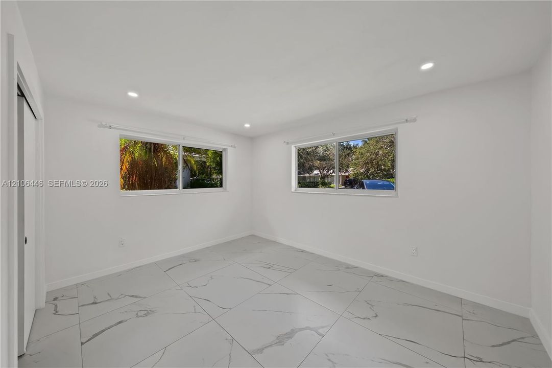 Neutral-toned interior featuring large-format, veined tile flooring, recessed ceiling lighting, and dual sliding windows