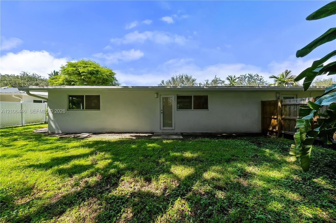 Rear exterior featuring a smooth-stucco facade, single-pane windows, a glass-panel entry door, and a partially fenced yard