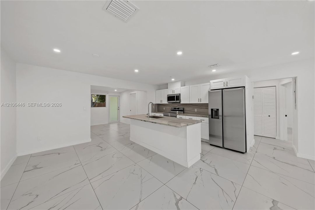 Kitchen featuring white cabinetry, an island with stone-finish countertop, recessed lighting, large-format tile flooring, and stainless steel appliances
