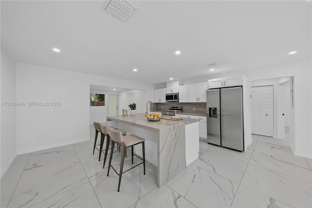 Kitchen featuring white shaker cabinetry, stainless steel appliances, a waterfall-edge kitchen island, and large-format tile flooring