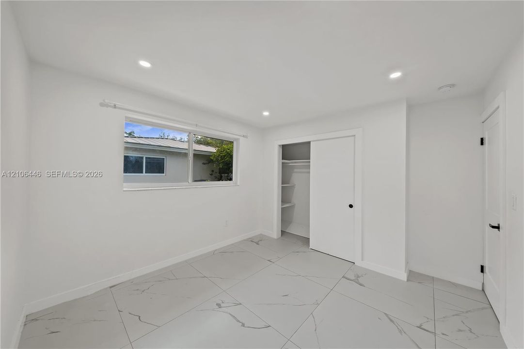 Large-format tile flooring with marble-style veining, recessed lighting, and a sliding-door closet with interior shelving