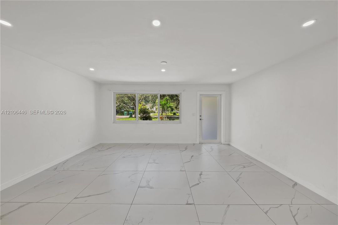 Open interior featuring large-format veined tile flooring, recessed ceiling lighting, a three-panel window, and a glass-paneled exterior door