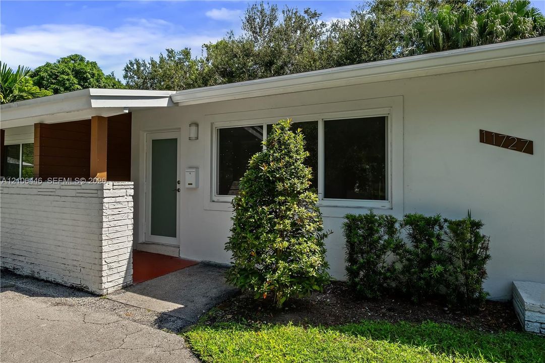 Exterior facade featuring a white-painted brick privacy wall, glass-panel entry door, and multi-pane windows