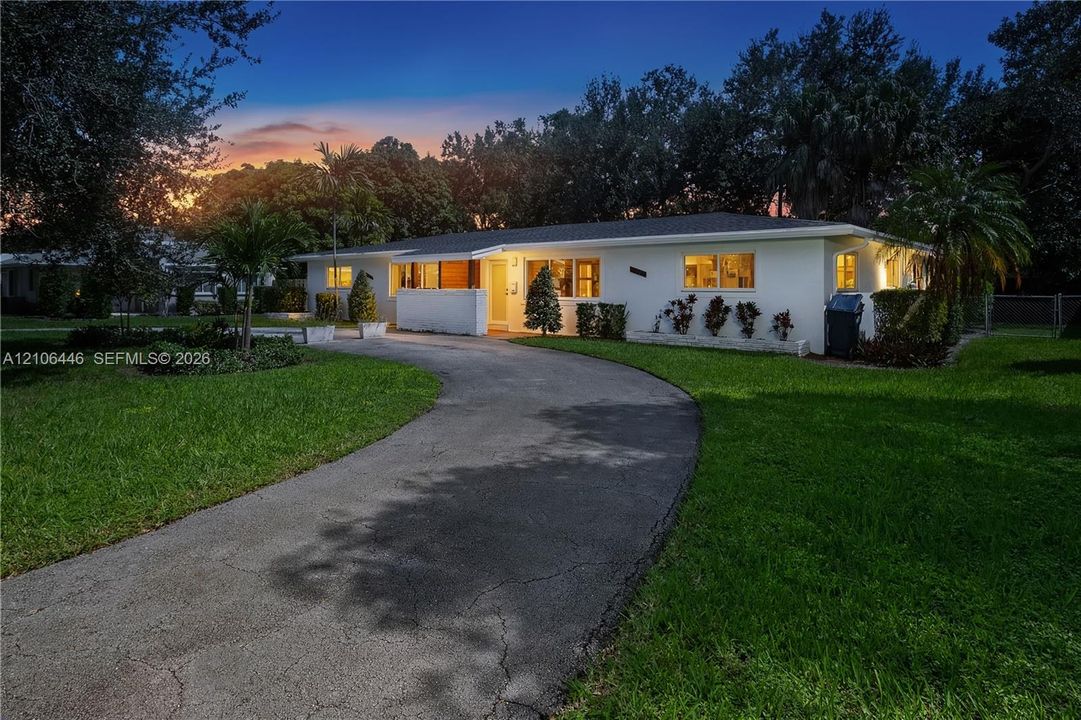 Single-story exterior featuring a light-colored finish, a sprawling front lawn, and a curved paved driveway