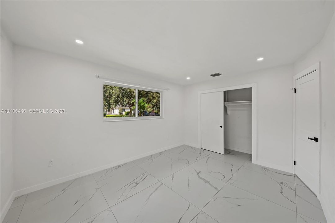 Large-format porcelain tile flooring, recessed LED lighting, sliding closet doors, and interior doors with matte black hardware