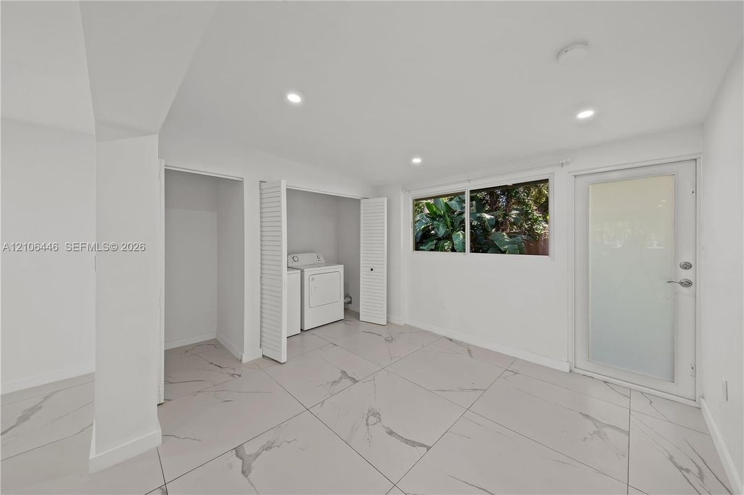Large-format tile flooring with veining detail, recessed ceiling lighting, built-in laundry closet with louvered doors, and exterior door with frosted glass panel
