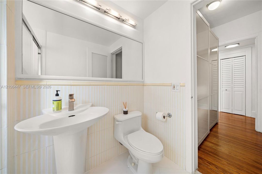 Bathroom featuring a pedestal sink, wall-spanning vanity mirror, light-toned vertical striped wall tile, and wood-finish flooring