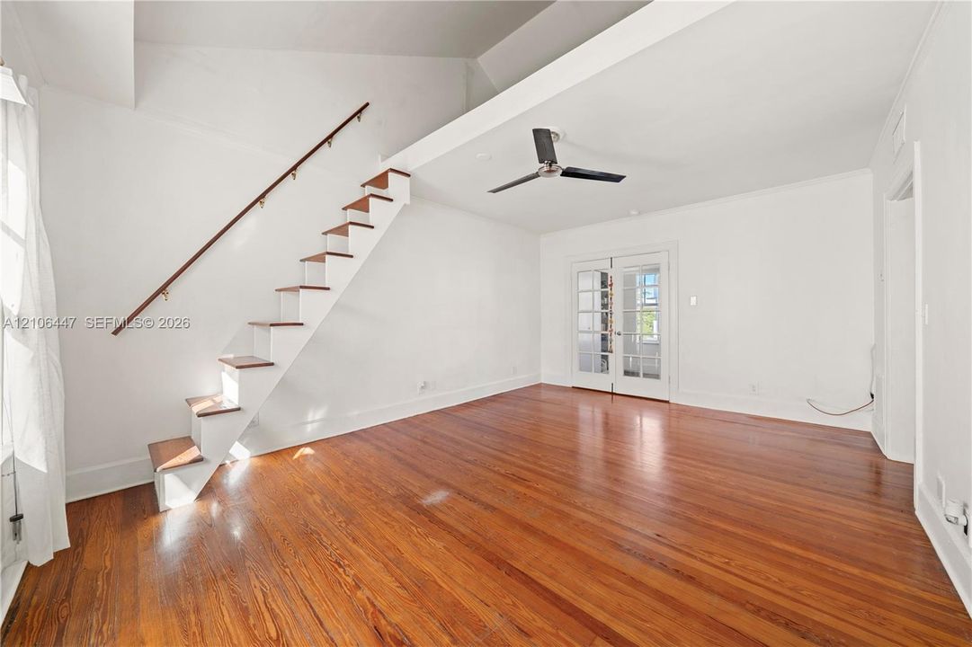 Vaulted ceiling, wood-finish flooring, staircase with wood treads and a metal handrail, ceiling fan, and French doors