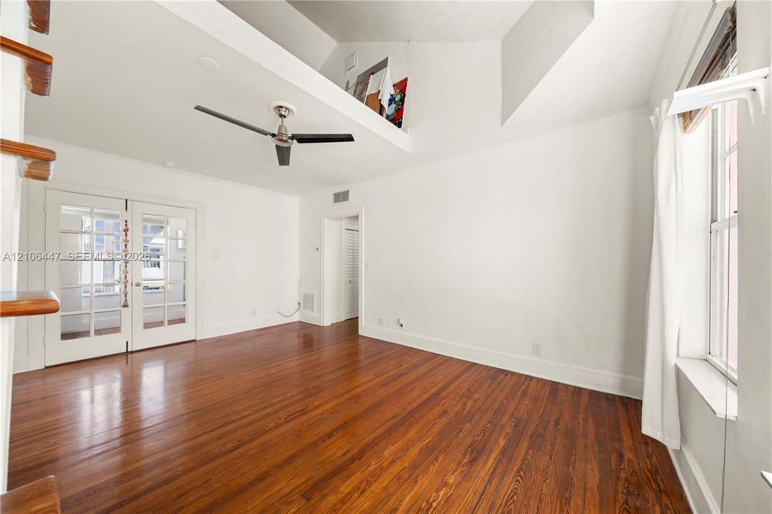 Vaulted ceiling with an integrated loft area, wood-finish flooring, multi-pane glass double doors, and a ceiling fan