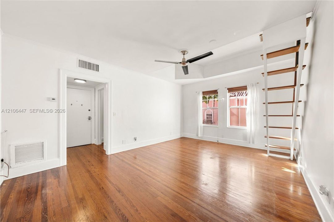 Living area featuring wood-finish flooring, a ceiling fan with integrated lighting, and a built-in ladder system